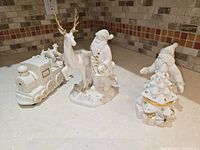 Porcelain set with Santa holding child and standing next to reindeer, and a holiday train figurine with gold accents on wheels and carrying toys.