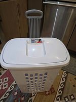 Front view of Sterilite white plastic laundry basket with white lid closed and extended trolley handle on patterned rug.
