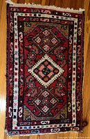 Full view of small rectangular Persian style area rug with geometric and floral patterns in red, white, pink and blue.