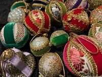 Close-up photo showing assortment of vintage Christmas ornaments with velvet and embroidered fabric, gold braid trim, and gold hanging cords.