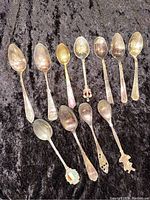 Photo showing 11 miniature collectible spoons arranged on black fabric, includes spoons with varying handle designs and colors