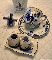 Close-up of teacup with saucer, salt and pepper shakers on tray, and windmill figurine showing traditional blue floral and windmill designs on white porcelain.