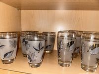 Eight vintage Libbey glasses with silver leaf decoration on a shelf, showing the collection and design consistency.