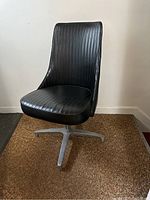 Front view of black vinyl MCM Chromcraft swivel bucket seat chair with vertical ribbing and metal base.