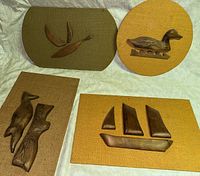 Four wooden wall art pieces displayed together showing bird, duck, dog, and sailboat sculptures on woven fabric backings