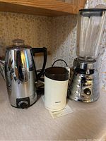 Osterizer Deluxe blender, Sunbeam percolator, and Krups grinder grouped on kitchen counter