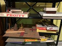 Shelf view showing Pegity, Scrabble, Mastermind, Bingo, stacking rings toy, Parcheesi board, and Twister board game boxes and boards.