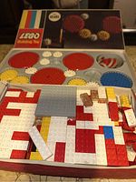 Open box view showing large gears and assorted Lego blocks inside with box lid propped in background.