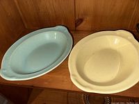 Pair of vintage Lu-RAY pastel oval dishes, one light blue and one pale yellow, shown side by side on a wooden shelf.