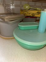 Photo of the collection showing boxed yellow salad tongs on top with turquoise cake keeper, large bowl, rectangular container, tall canister, and stacked beige containers.
