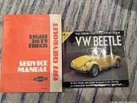 Photo showing the front covers of the two books: the 1977 Chevrolet Light Duty Truck Service Manual with a red and gray cover and The Origin and Evolution of the VW Beetle book with a yellow VW Beetle car on the cover.