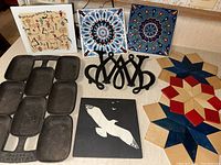 Overview photo showing cast iron baking pan, Wm & Mary cast iron trivet, woven wooden hot pads in red and blue, and decorative tiles including bird silhouette and intricate patterns.
