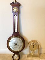Full view of vintage Airguide banjo barometer and Seiko quartz desk clock on floor against wall