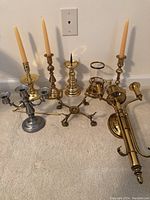 Full view of four brass candlesticks, two brass candleholders, a brass wall sconce, silverplate candelabra, candle snuffer, and tea lights.