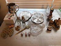 Full view of all items on fabric surface under window blinds showing the entire lot including metal, glass, and figurine items.