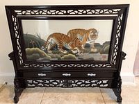 Side of framed embroidered textile showing two tigers in natural setting with carved wood stand