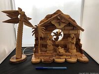 Full view of olive wood nativity stable with figurines and detached lighted palm tree on side, showing natural wood texture and details.