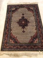 Full view of wool area rug showing the overall pattern of a dark central medallion and diamond motifs on cream field with colorful border and fringe.