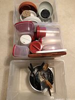 Overhead view of plastic storage containers with lids, some round and some rectangular, stacked inside a clear bin with cutting boards underneath and some other kitchen items.