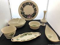 Photo showing five cream-colored holiday dishes with holly leaf and berry designs alongside one white Lenox bud vase.