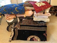 Stack of various throws, pillow covers, and towels arranged showing different textures and patterns including moon print and floral designs.