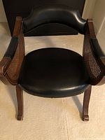 Front view of vintage occasional chair showing black upholstered seat and backrest, wooden frame, and wicker panel sides.