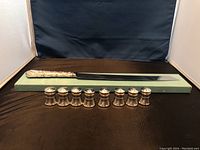 Fourteen items displayed on brown surface with a dark backdrop. Eight pewter salt and pepper shakers lined up in front with sterling handle cake slicer behind them.