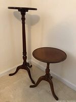 Pair of wooden plant stands, one tall with slender pedestal, the other shorter and round-topped.