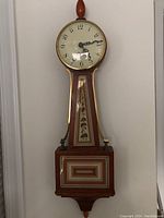 Full front view of the Seth Thomas banjo wall clock showing its oval clock face, wooden case with painted details, and finial top.