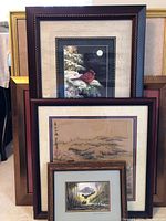 Group photo showing five framed artworks stacked against a wall, featuring varied sizes and styles, prominently a cardinal bird image.
