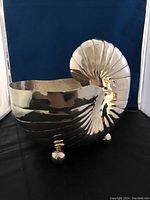 Silverplate champagne chiller shaped like a nautilus shell, showing polished exterior and round feet.