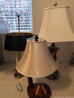 Three table lamps shown together; one with a white shade and wooden base with pyramid decoration, two with brass bases and black and cream shades.