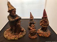 Overview of the four Tom Clark gnome sculptures of different sizes on a flat surface indoors.