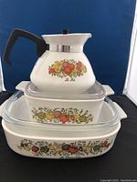 Set of vintage CorningWare kitchen pieces including teapot and two casserole dishes stacked and visible design details.