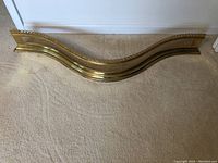Full view of brass fireplace fender with curved shape on beige carpet