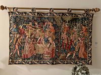 Full frontal image of the tapestry hung on a rod with decorative finials, showing the detailed medieval winemaking scene with multiple figures and grapevines.