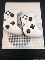Xbox One S console top with two white Xbox wireless controllers placed on top showing button layout and console ventilation.
