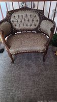 Antique Victorian loveseat in beige patterned fabric with carved wooden frame and button tufting