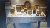 Photo showing a collection of approximately 18 assorted picture frames on a table, various sizes and frame materials visible.