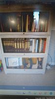 Front view of a wooden sectional bookcase with three glass-door compartments showing book storage inside. The photo captures the overall condition and structure of the piece.