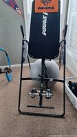 Black inversion table with padded backrest, foot supports, and sturdy frame positioned in room corner.