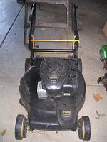 Front view of gas mower showing top of engine and foldable handle secured with yellow lock.