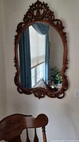 Antique wood carved oval wall mirror hanging on wall with a dark finish featuring floral and scrollwork details in the frame.