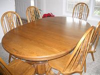 Full angle showing oak oval dining table with 8 oak chairs arranged around it, revealing pedestal base and wood grain finish.