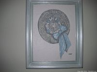 First oil painting showing a woven hat with blue ribbon and floral decoration on a beige background, framed in silver.