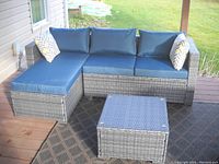 Outdoor grey wicker L-shaped sectional sofa with blue cushions and two accent pillows featuring a chevron pattern, viewed from side angle on patio deck.
