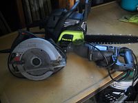 Photo showing a Poulan chainsaw, a circular saw marked 21V, and a black/grey reciprocating saw on a table.