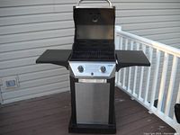 Front view of a 2 burner propane grill with open lid, metal grates, two control knobs, and two side shelves on a wooden deck.
