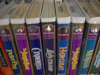 Close-up of the spines of several VHS tapes revealing titles such as Peter Pan, Cinderella, Lady and the Tramp, Hercules, and The Little Mermaid