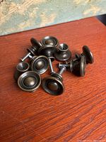 Photo of all 10 brass knobs with dark distressed finish piled on a wooden surface showing round shape and metal screws attached.